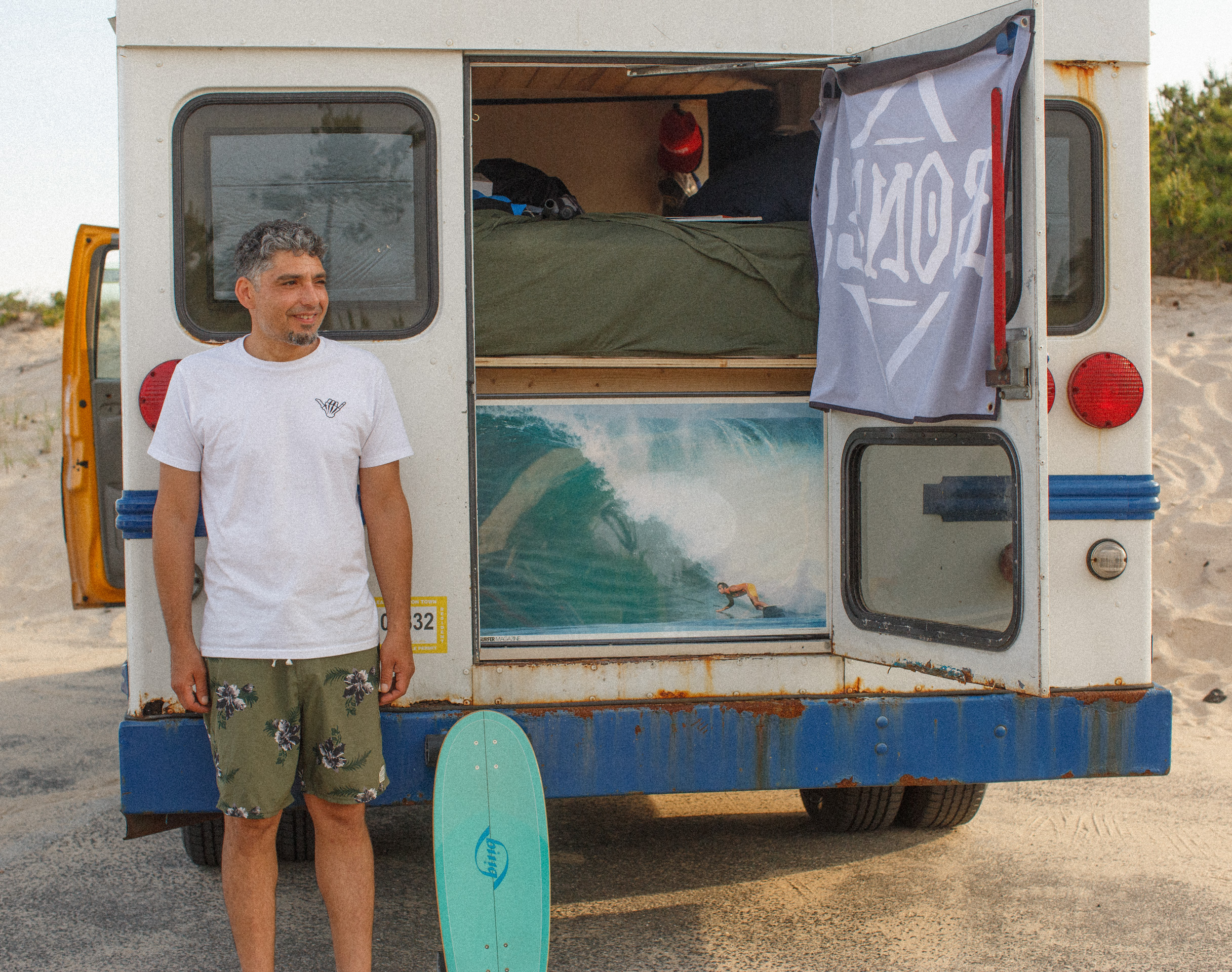 Monte, Strictly Surf owner and instructor, beside the surf bus with a softboard