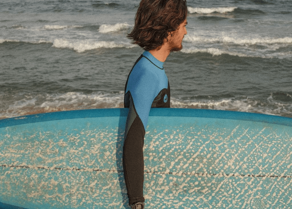 Surfer in a wetsuit walking with a board down to the beach