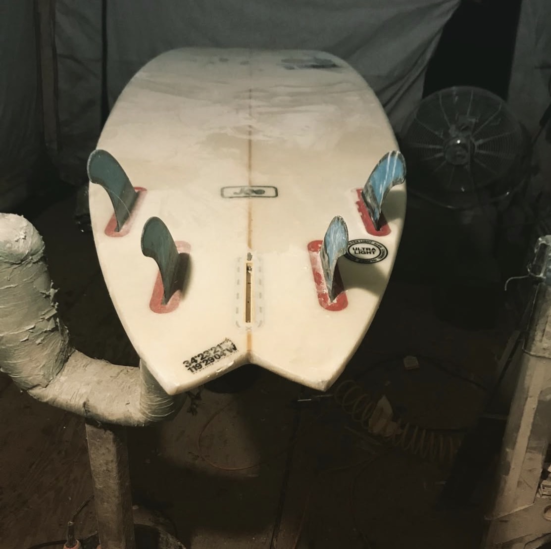 Fish surfboard tail with fins resting on the workshop bench